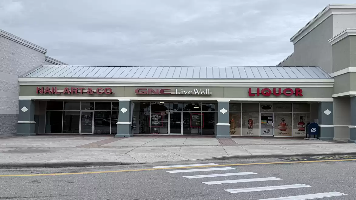 Shopping center with signs for a nail salon, pharmacy, and liquor store on a cloudy day.