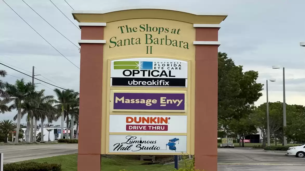 Entrance sign for 'The Shops at Santa Barbara II' shopping mall with various stores including an optical shop, Massage Envy, and Dunkin'.