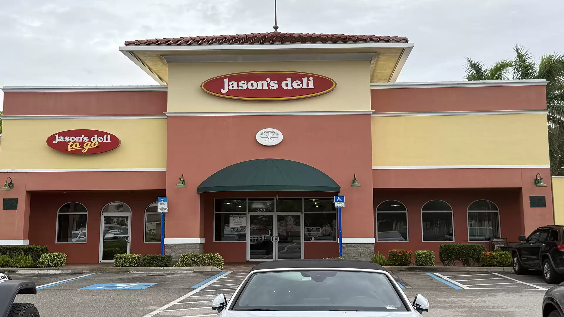 An exterior view of a deli named 'Jason's Deli' in a single-story building, surrounded by parked cars.