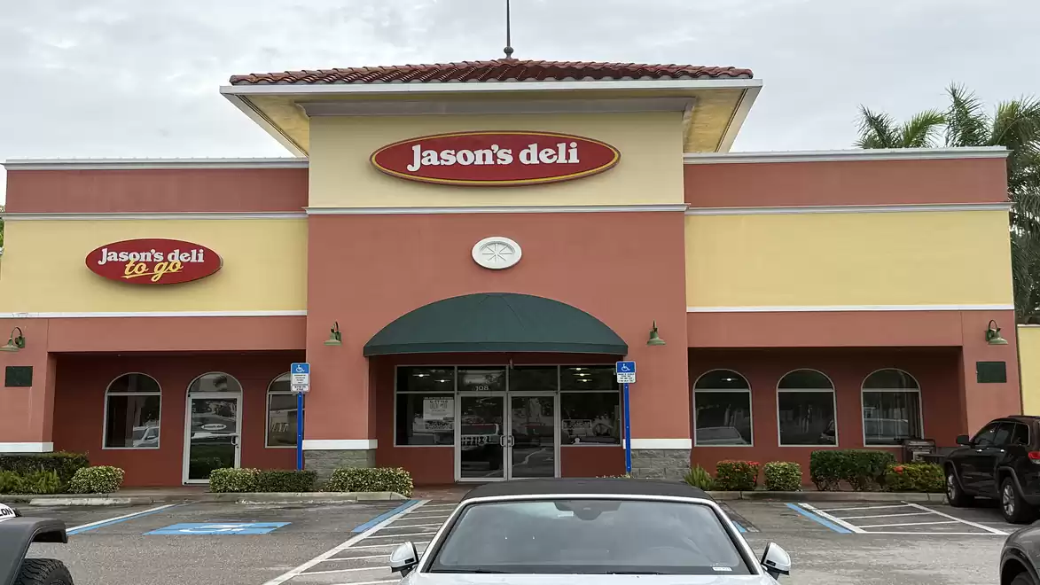 An exterior view of a deli named 'Jason's Deli' in a single-story building, surrounded by parked cars.