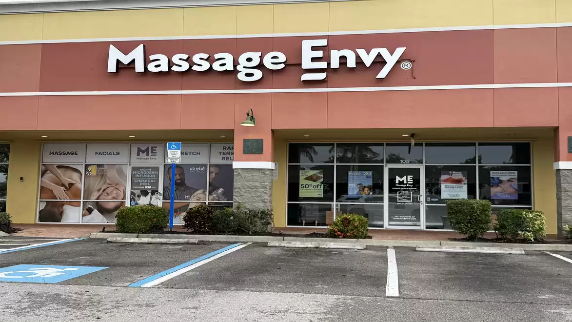 Exterior view of a Massage Envy studio with parked cars and plants.