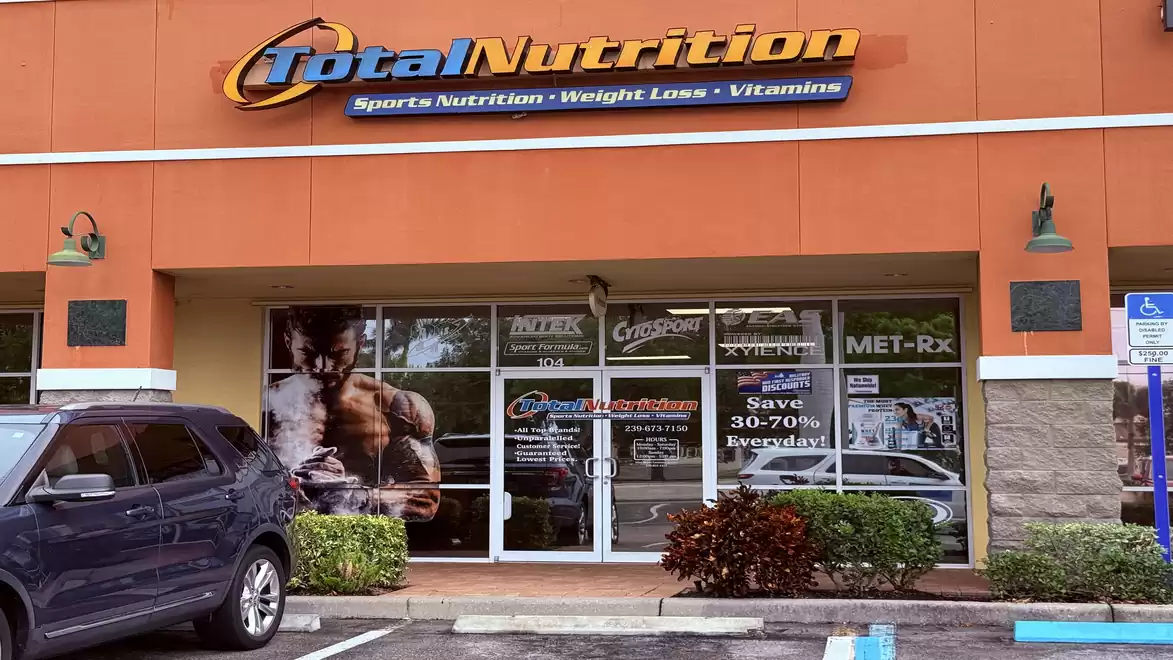 Exterior view of a specialty store for sports nutrition and vitamins, featuring a large advertisement poster of a muscular man in the window.
