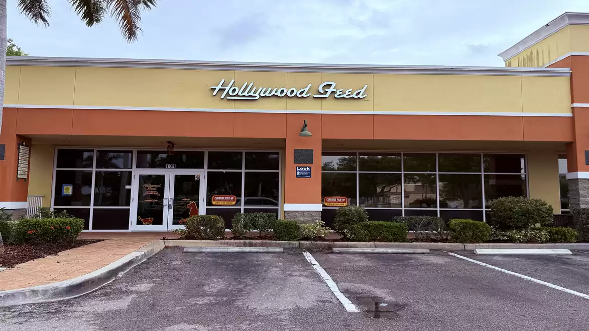 A store with the sign 'Hollywood Feed' on the facade. The building has a yellow and orange paint with large windows. The parking lot in front is empty.
