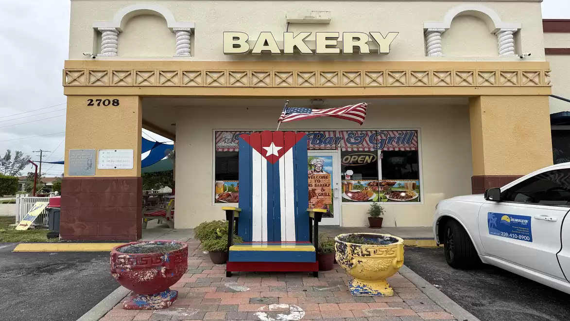 A bakery with Cuban flag and colorful decorations, featuring a large, vibrant chair in front.