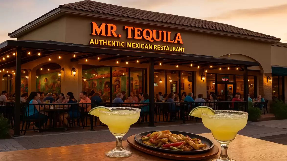 Exterior view of a Mexican restaurant at sunset with guests on the terrace and two margaritas in the foreground.