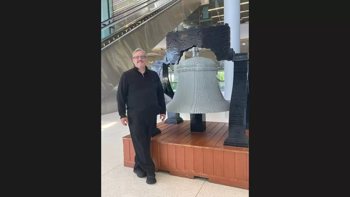 Man standing next to a large bell in a modern building.