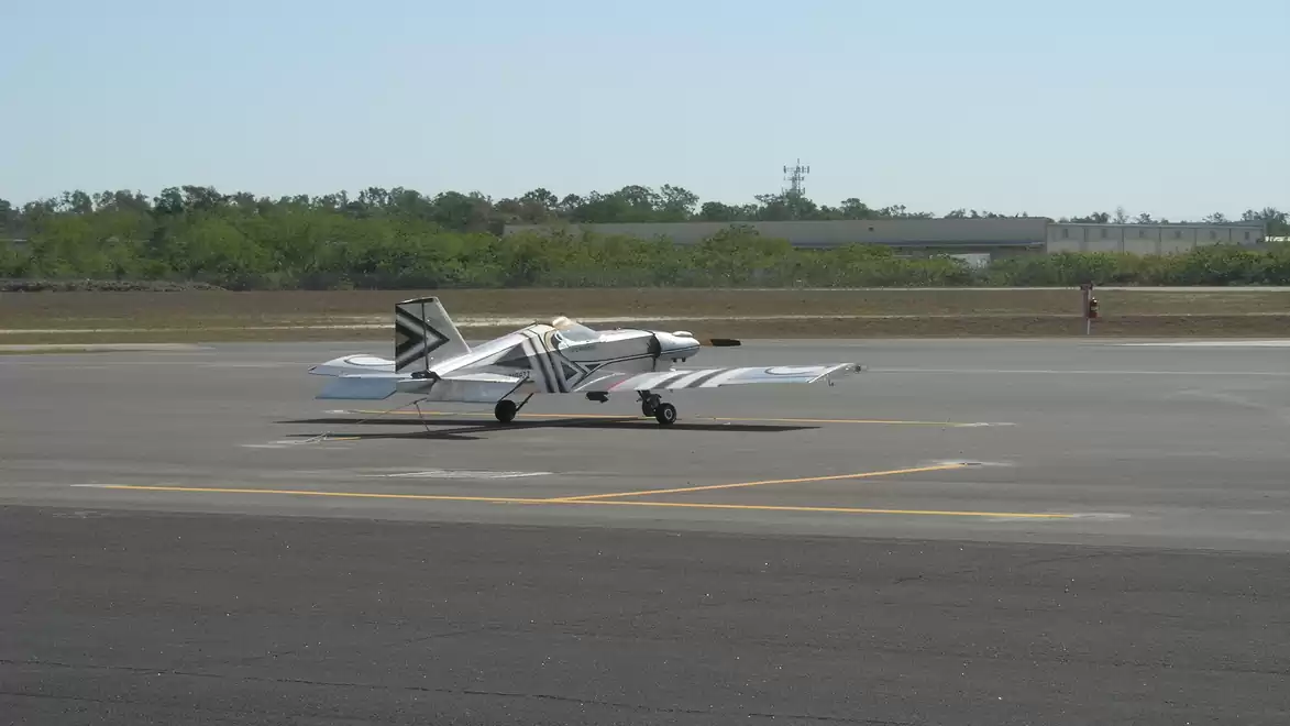 Small aircraft with black and white stripes on a runway on a sunny day.