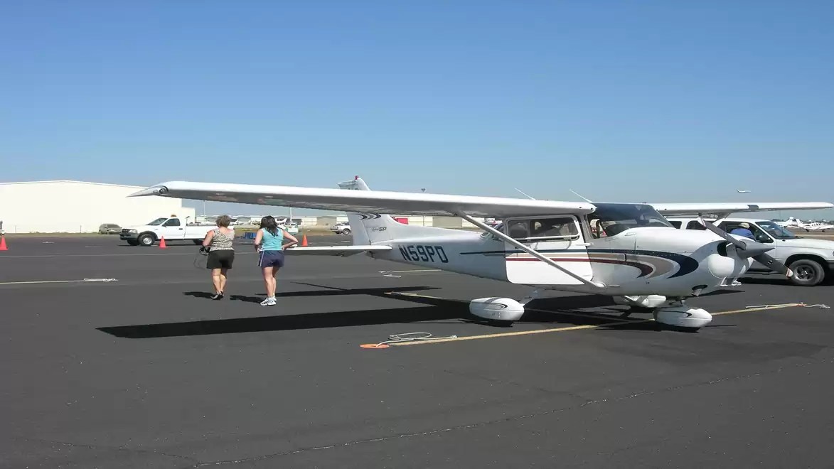 Small airplane at an airport with two people walking beside it.