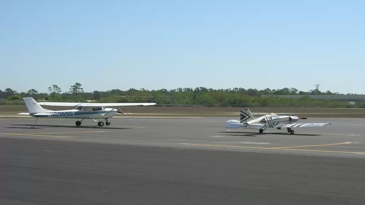 Two small airplanes on an airport tarmac, ready for takeoff under the blue sky.