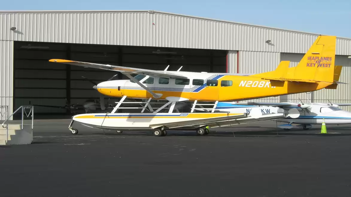 Yellow seaplane parked in front of a hangar at an airfield.
