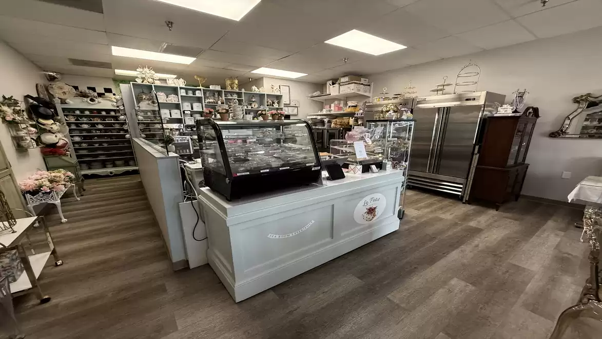 Interior view of a cozy bakery and pastry shop with display cases full of treats, shelves with baking ingredients and kitchen equipment in the background.
