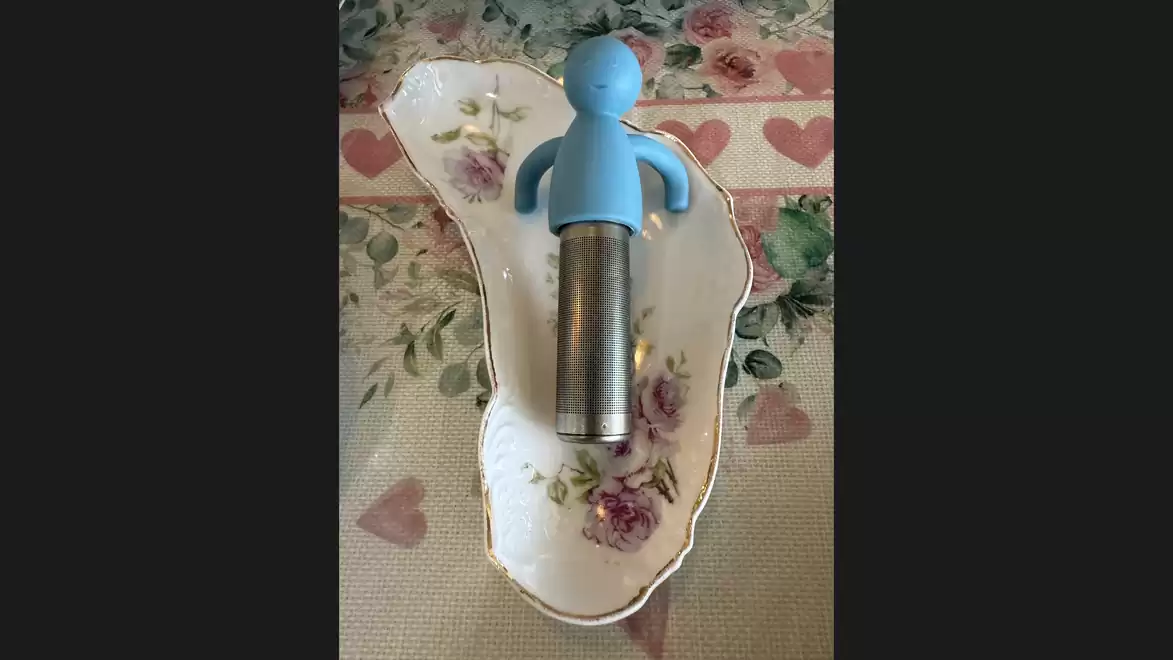 A blue corkscrew with a human-like figure lies on a floral-decorated porcelain plate.