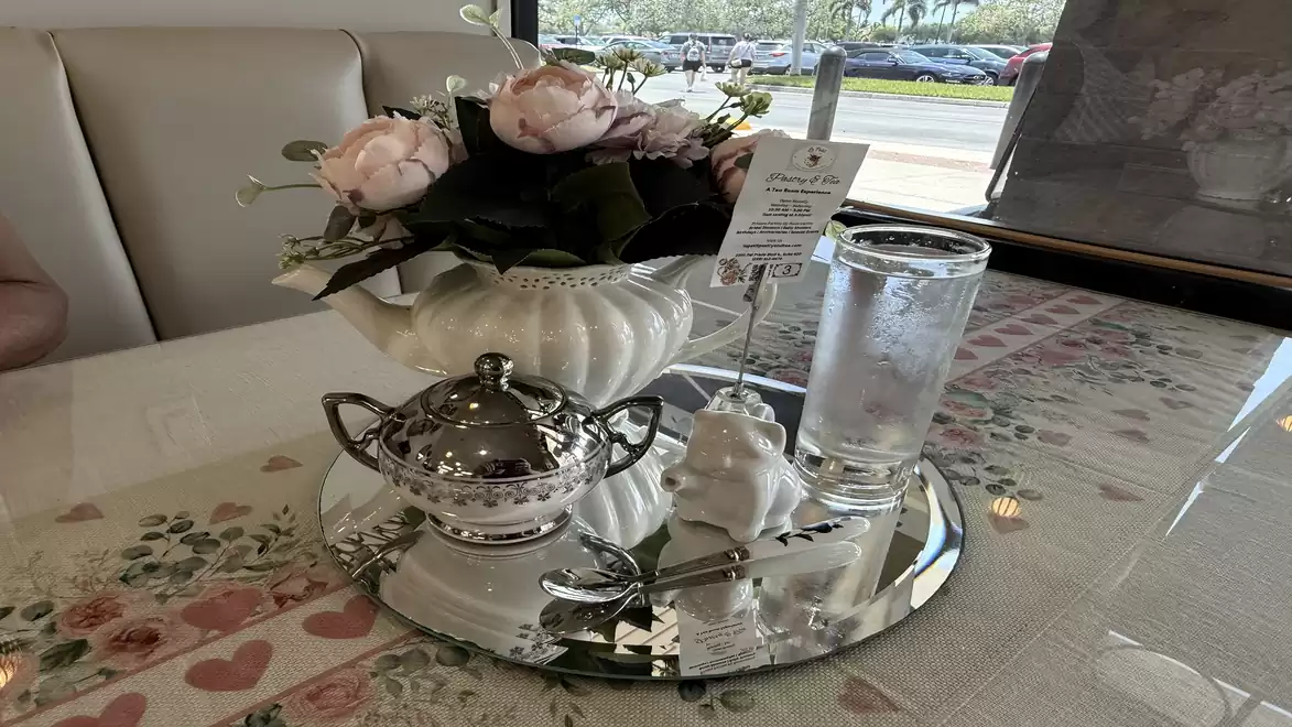 A table in a café with a floral arrangement, a glass of water, a sugar dispenser, and a menu on a mirrored tray.
