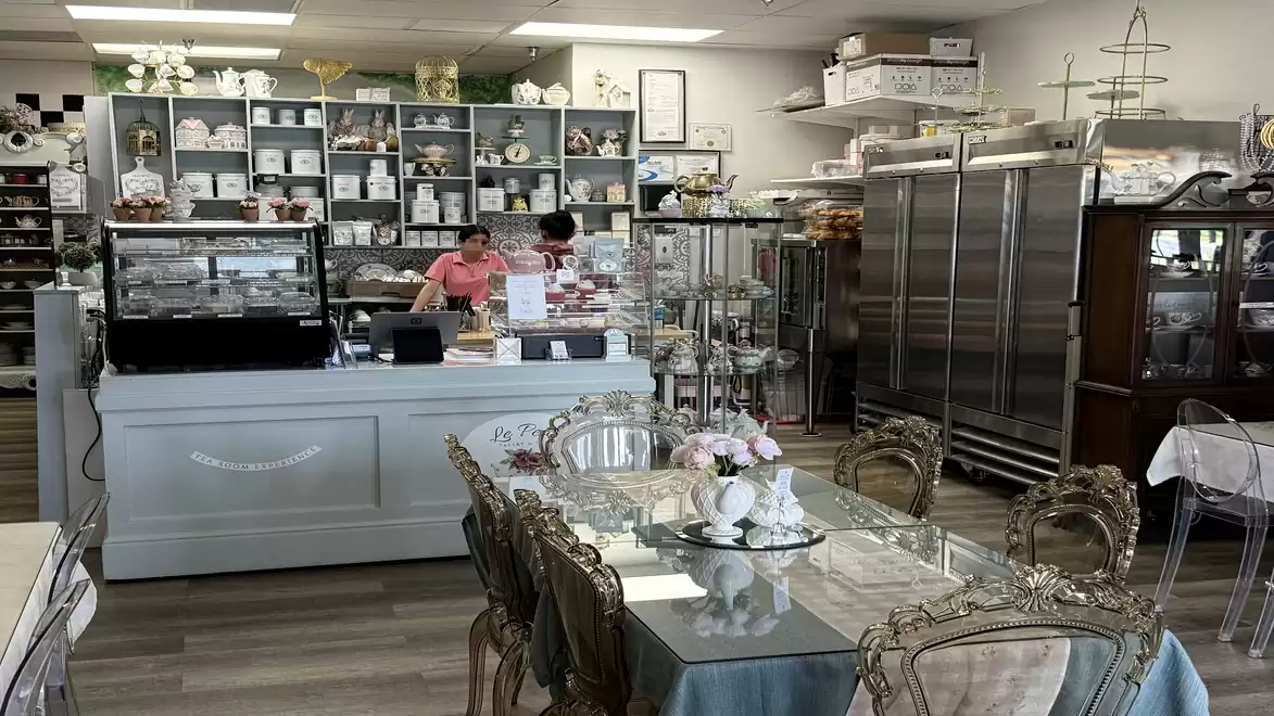 A cozy café with decorative furniture and shelves full of dishes. Two people are working behind the counter.