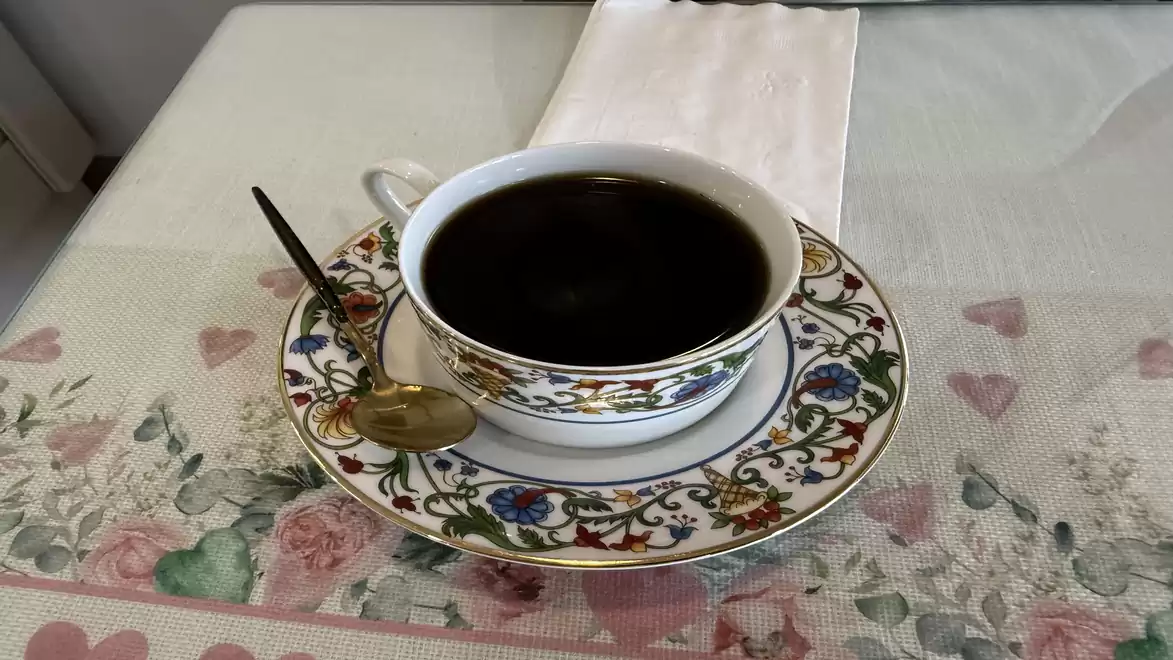Elegant cup of black coffee on an ornately decorated saucer, set on a floral-patterned tablecloth.