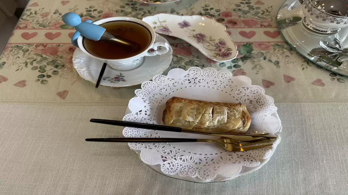 An elegant table featuring tea in a fine cup and a pastry on a decorative plate with lace underneath, accompanied by golden and black chopsticks.
