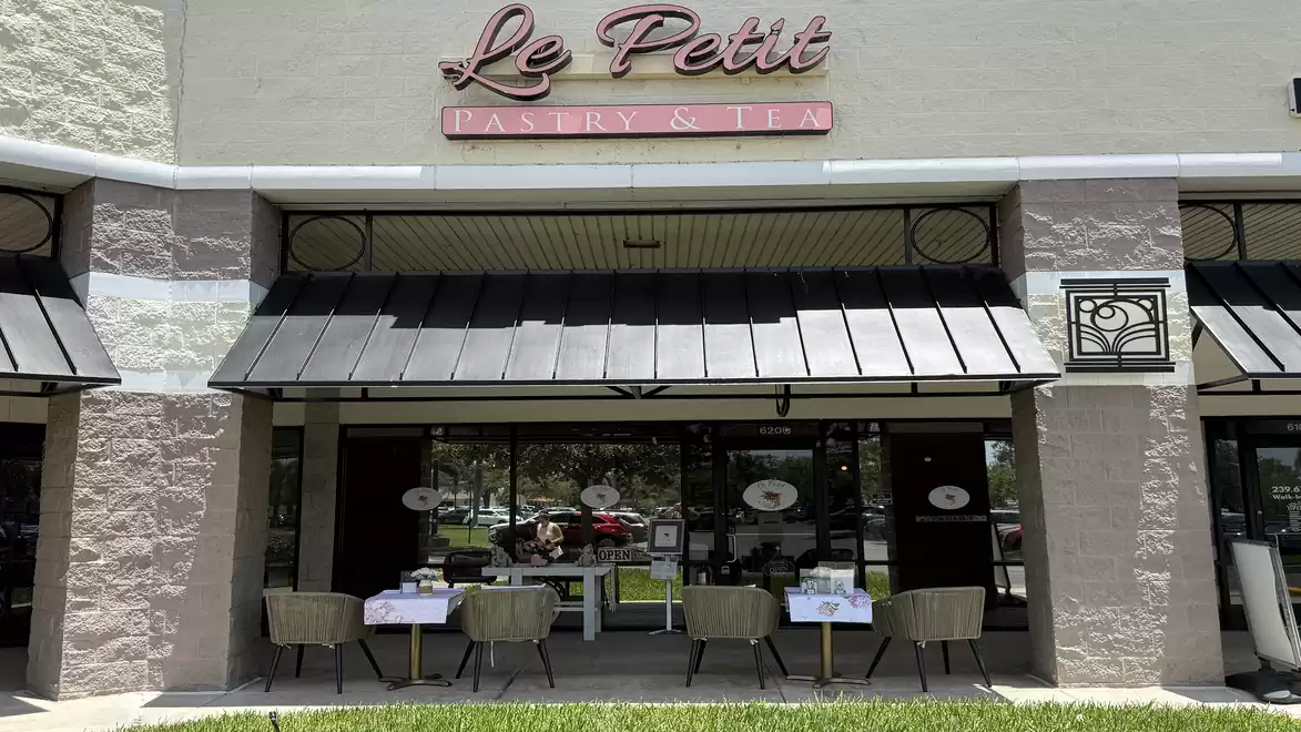 Exterior view of a small café named 'Le Petit Pastry & Tea', with outdoor chairs and table.