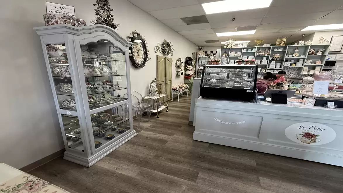Interior shot of a small shop with white decor, a glass display cabinet filled with items, and a sales counter surrounded by shelves stocked with various goods.