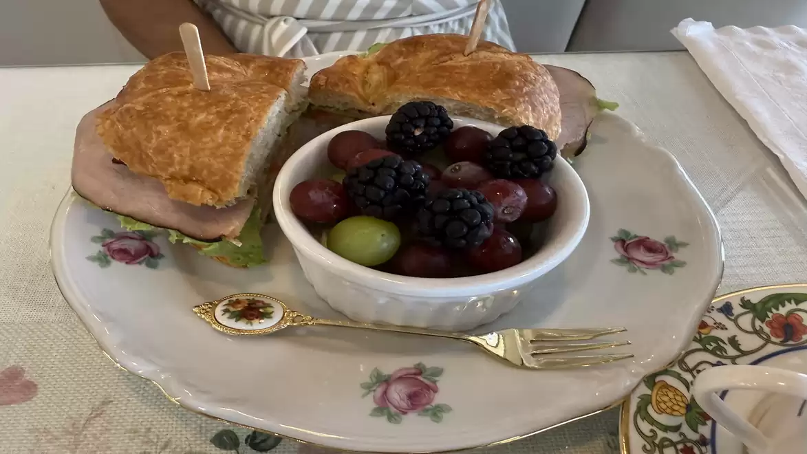 A plate with a sandwich filled with meat and lettuce, next to a bowl of grapes and blackberries. The dishware is decorated with floral patterns.