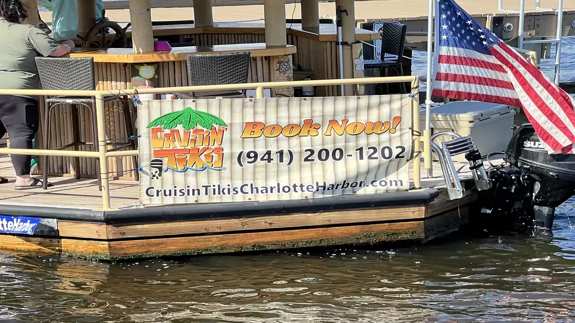 A floating tiki boat on the water with an advertisement banner and an American flag.