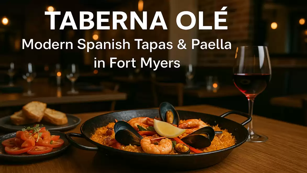 A plate of Spanish paella, garnished with seafood, a lemon wedge, and mussels, is on a wooden table in a restaurant. In the background, a glass of red wine and blurred table decorations are visible. The text above reads 'TABERNA OLÉ Modern Spanish Tapas &