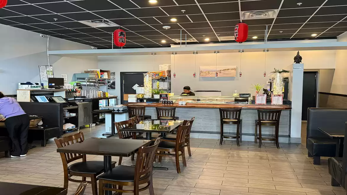 Interior view of a modern restaurant with several tables and chairs. A counter is in the background and red lanterns hang from the ceiling.