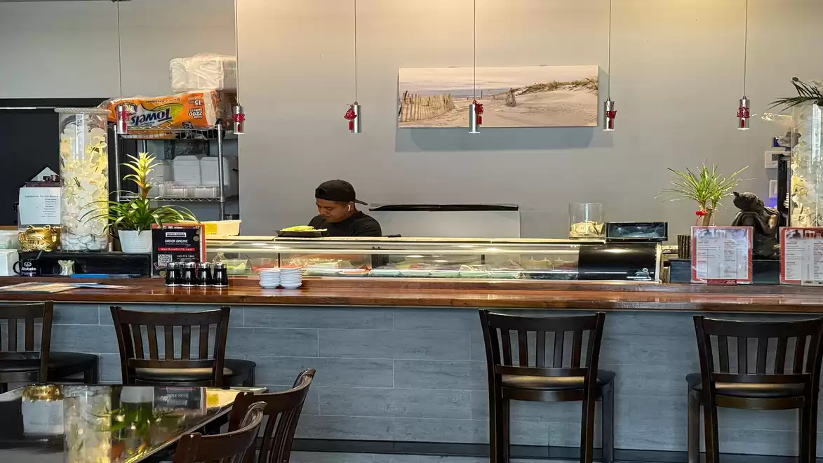 A restaurant with a sushi counter, where an employee is standing; wooden counter and modern decoration.