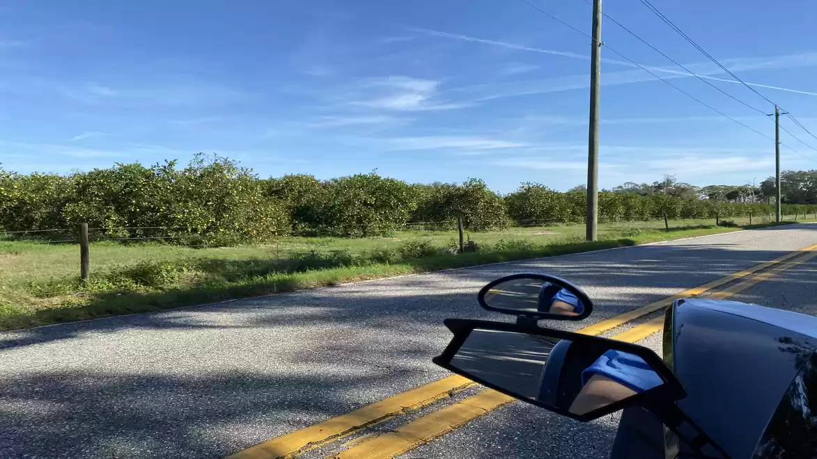 Rural road with a car and green fields under a blue sky.