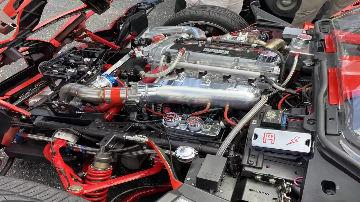 Photo of an open sports car engine bay with a clean, shiny engine, red accents, and numerous components.