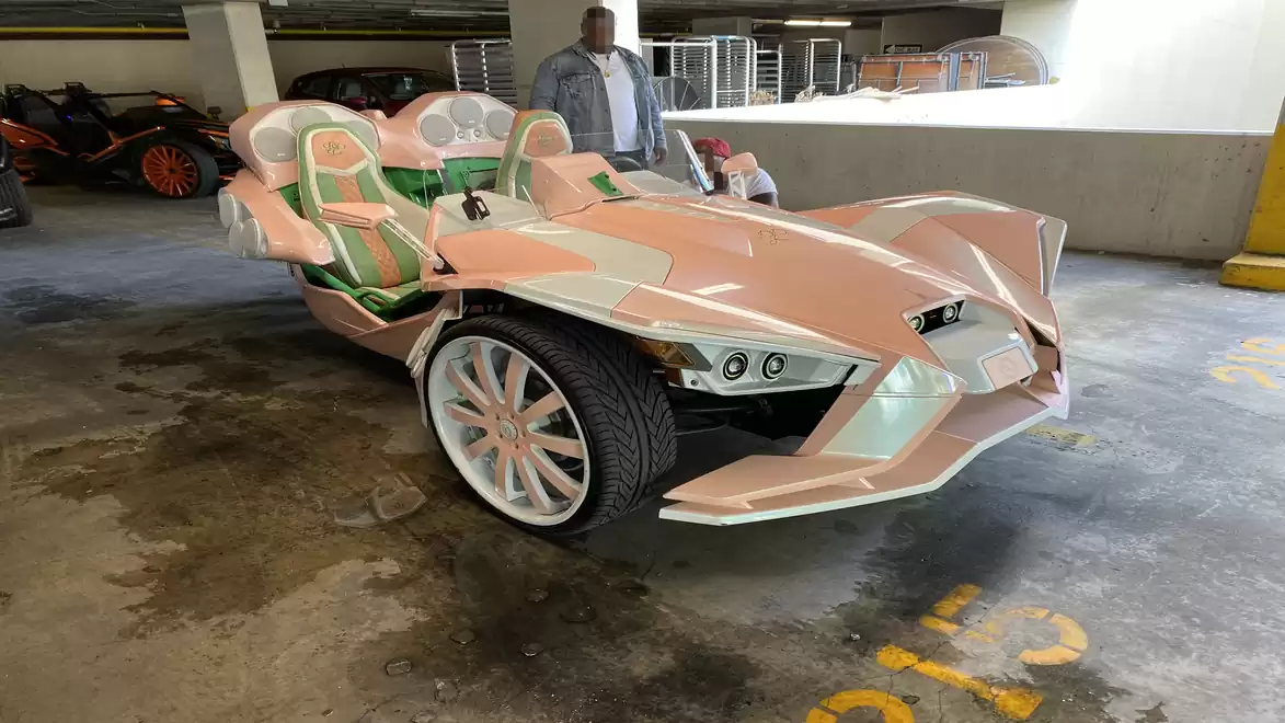Three-wheeled, pink and white vehicle with a sporty design parked in a parking garage.
