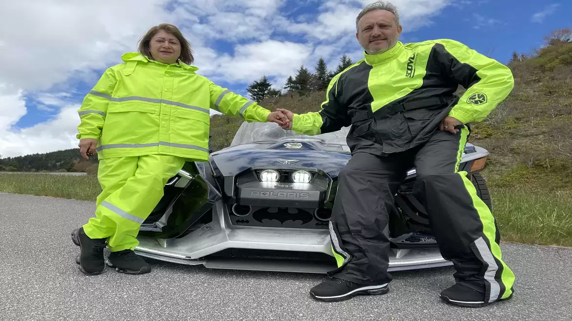 Two people in bright yellow motorcycle gear posing in front of a modern motorcycle on the roadside.