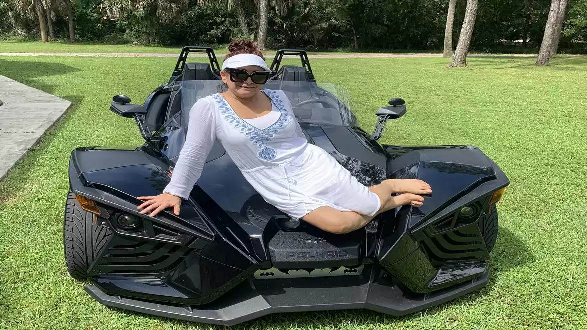 Woman in a white dress sitting on a black three-wheeled vehicle on a lawn.