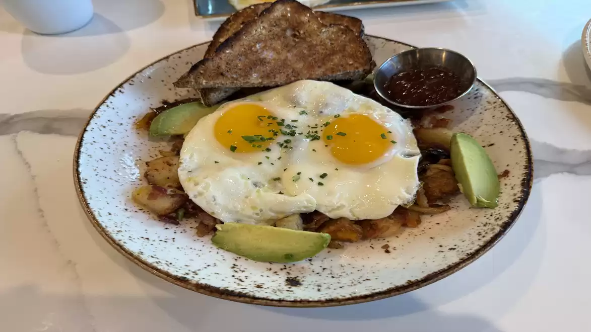 Breakfast plate with fried eggs, avocado, roasted potatoes, and toast on a rustic plate.