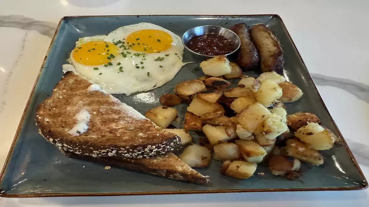 Breakfast plate with two fried eggs, hash browns, sausage, and toast.