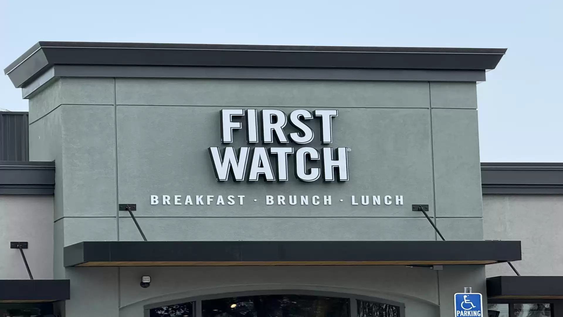 Exterior view of a restaurant named 'First Watch' offering breakfast, brunch, and lunch. A handicap parking sign is visible.