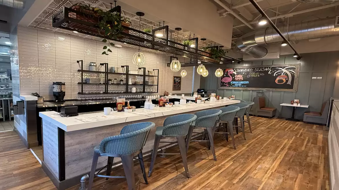 A modern café with a long white counter and blue chairs, surrounded by stylish decor and cozy lighting.