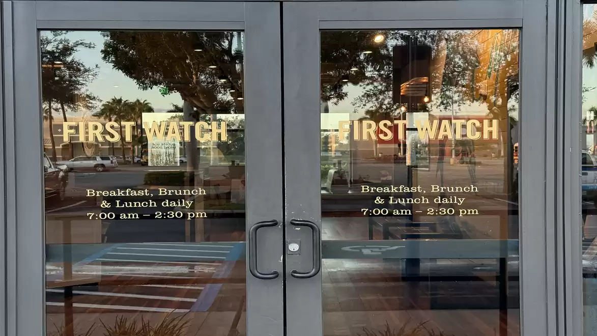 Restaurant entrance with two glass doors labeled 'First Watch' and opening hours for breakfast, brunch, and lunch.
