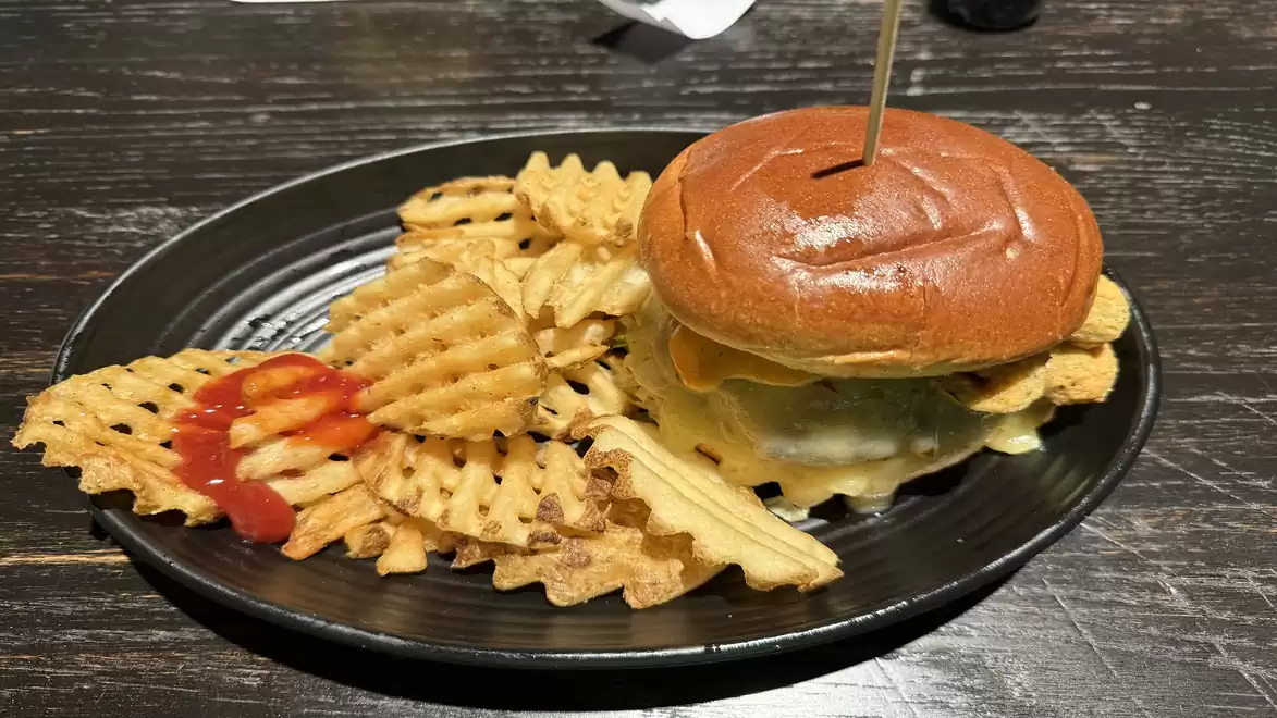 A juicy cheeseburger with waffle fries and ketchup on a black plate.