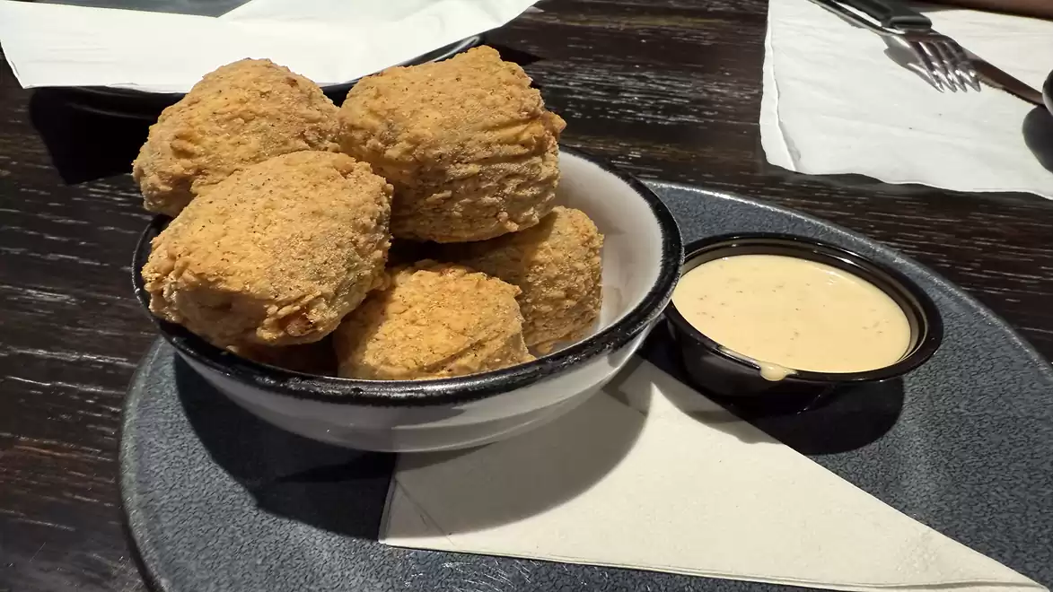 A plate with several golden-brown biscuits with pork and a small cup of dipping sauce on a table.
