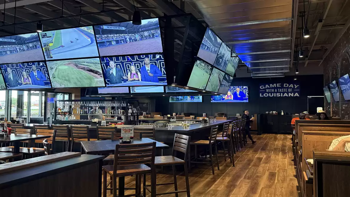 Interior view of a modern sports bar with several large TVs on the walls and wooden furniture.