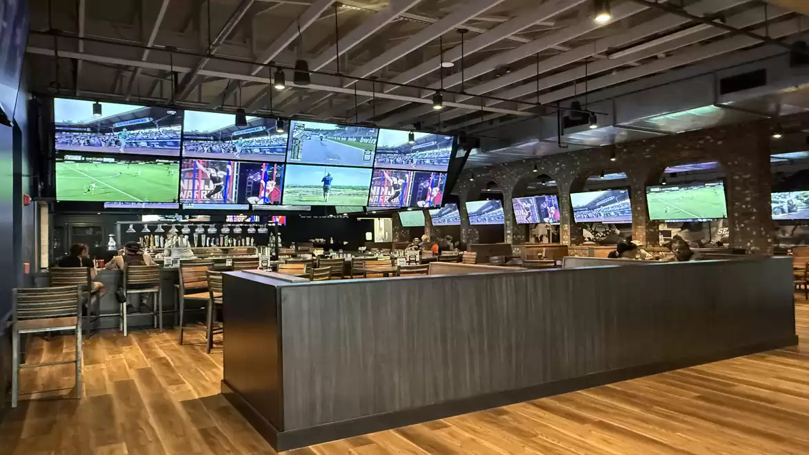Sports bar with multiple TVs showing various sports events and a modern, spacious interior with a bar area.