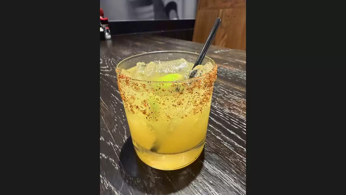 A glass of a refreshing drink with ice cubes, garnished with lime slices, on a dark wooden table.