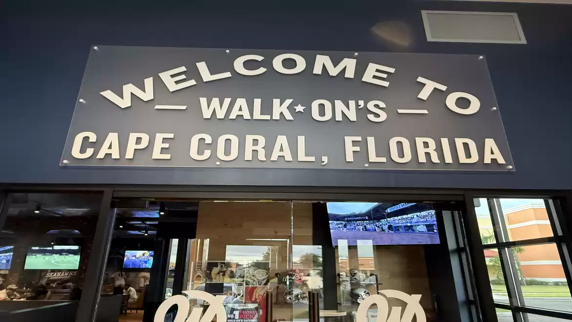 Entrance of a restaurant with a large sign reading 'Welcome to Walk-On's Cape Coral, Florida'.