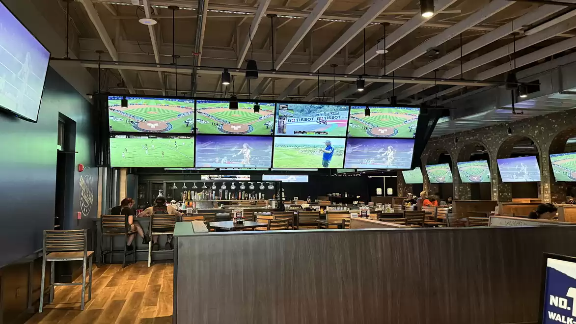 Sports bar with multiple screens showing a baseball game. Cozy seating and several TVs on the walls.