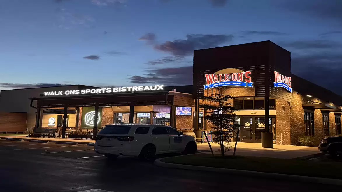 Exterior view of a sports bistreaux at dusk with illuminated signs and a parked car.