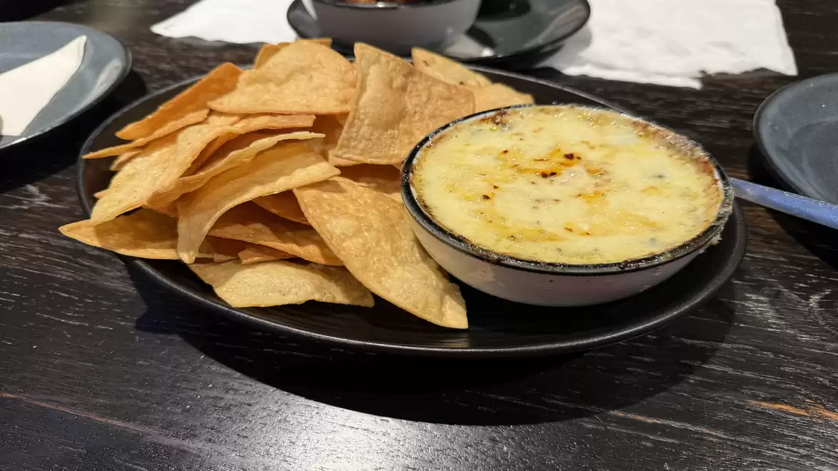 A plate of tortilla chips next to a bowl of hot, melted cheese, served on a dark wooden table.