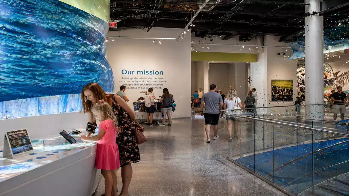 A modern museum with visitors exploring interactive exhibits and a wall with the words 'Our mission'.