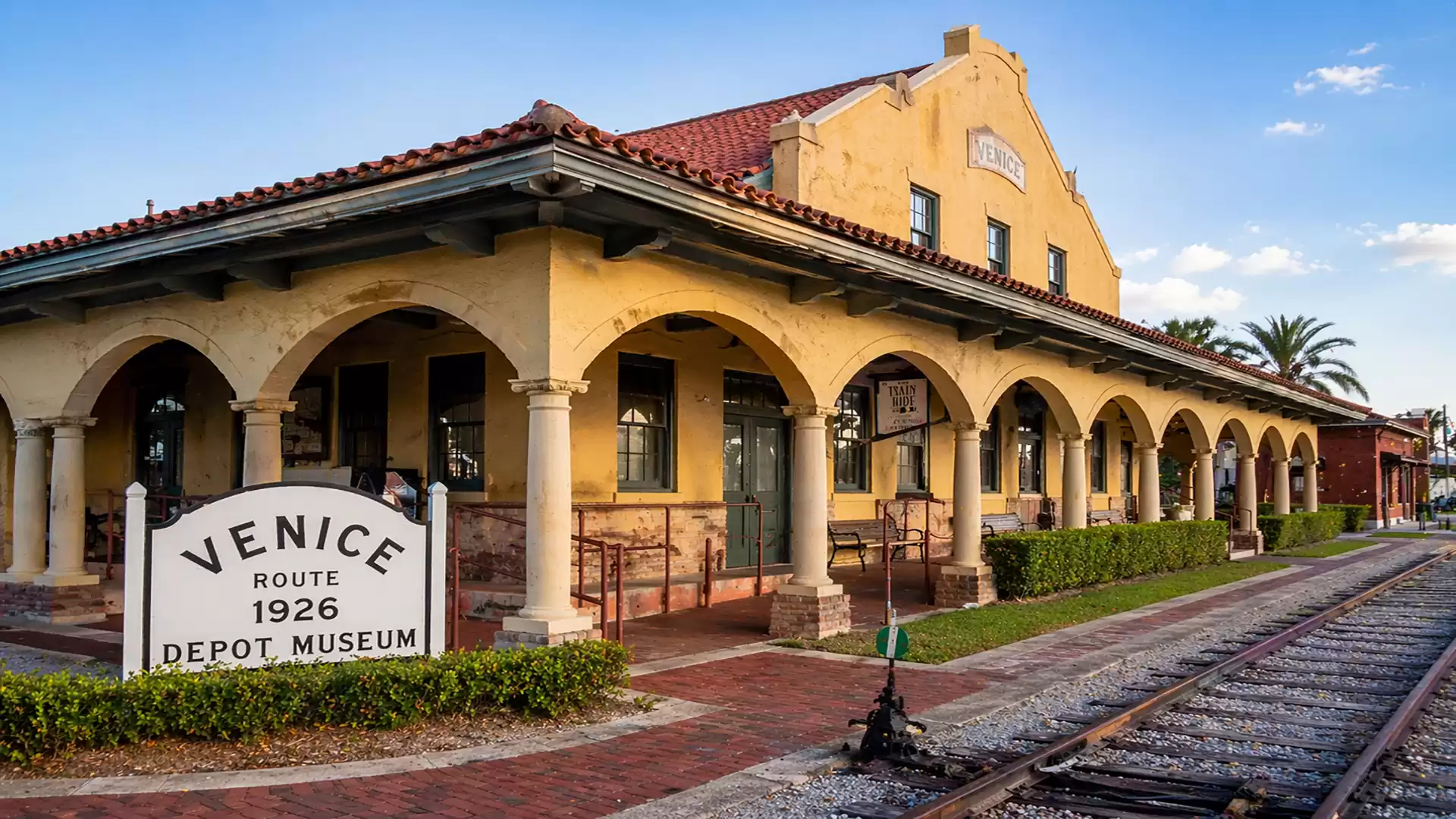 Historic Venice Depot Museum building with arcades at sunset, tracks in foreground, Florida.