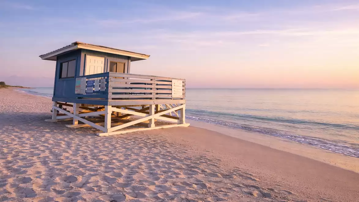A blue lifeguard tower on a calm sandy beach at sunset.