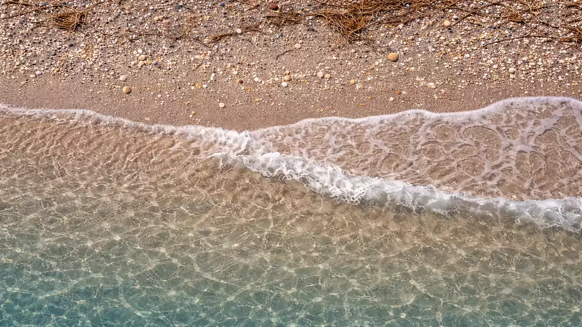 Aerial view of a calm beach with clear waves and pebbles on the shore.